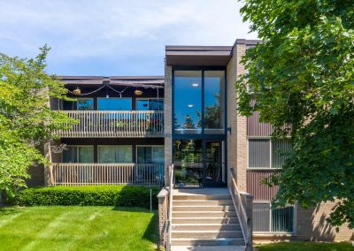 Outside view of river drive apartments with front entry, trees and a sunny skie