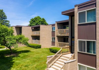 Outside view of river drive apartments with front entry, trees and a sunny skie