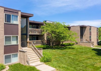 Outside view of river drive apartments with front entry, trees and a sunny skie