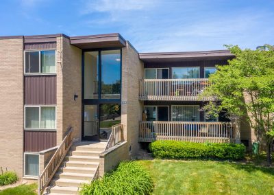 Outside view of river drive apartments with front entry, trees and a sunny skie